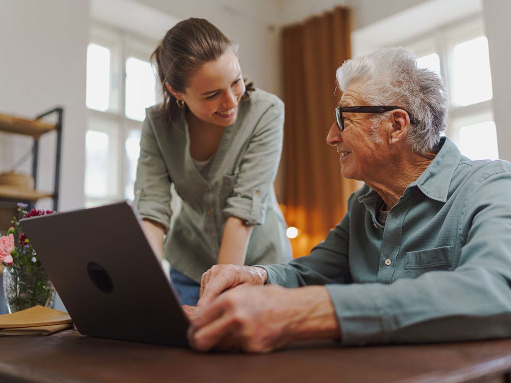 carer_helps_senior_elderly_man_laptop_computer