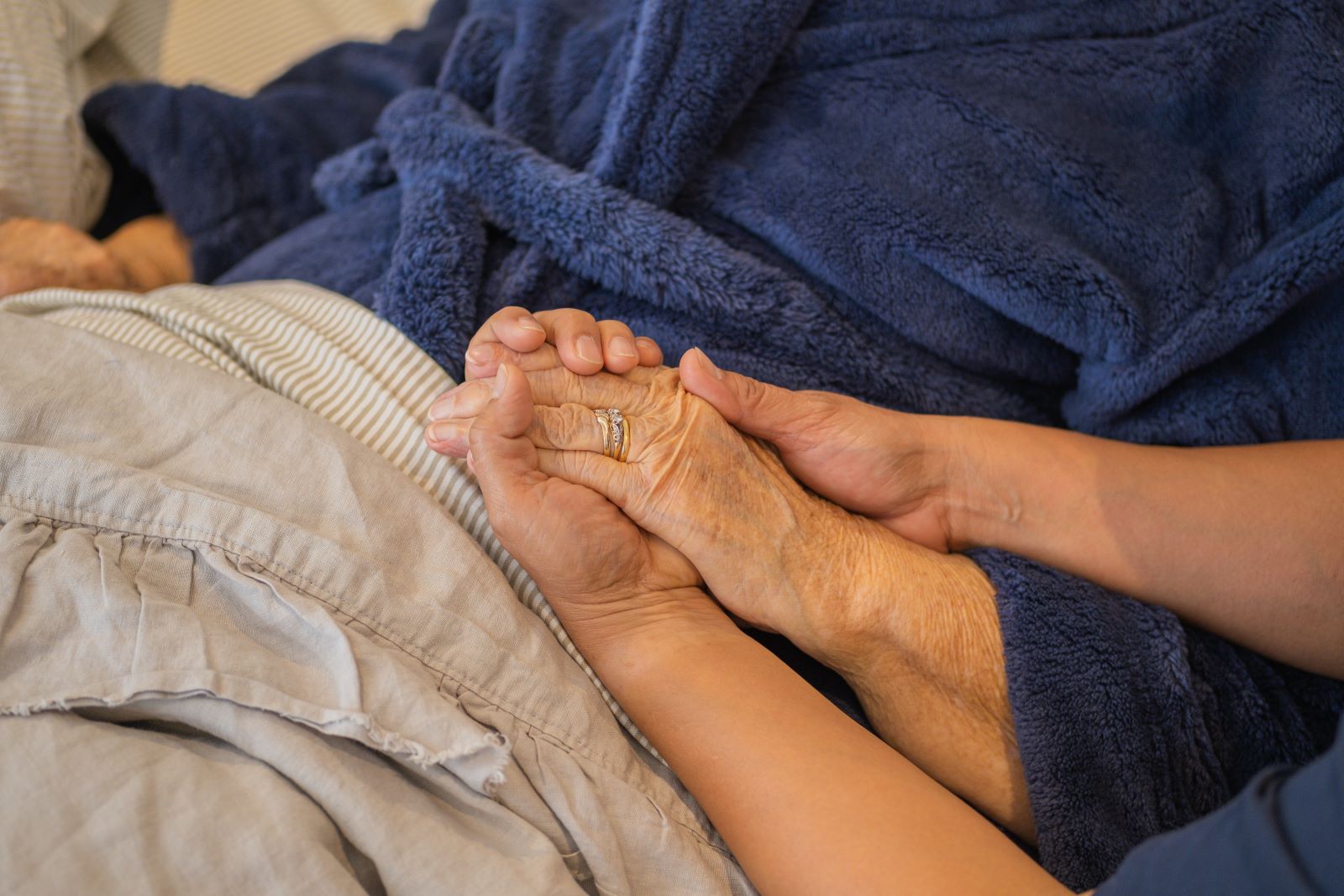 A woman holds the hand of an elderly woman.