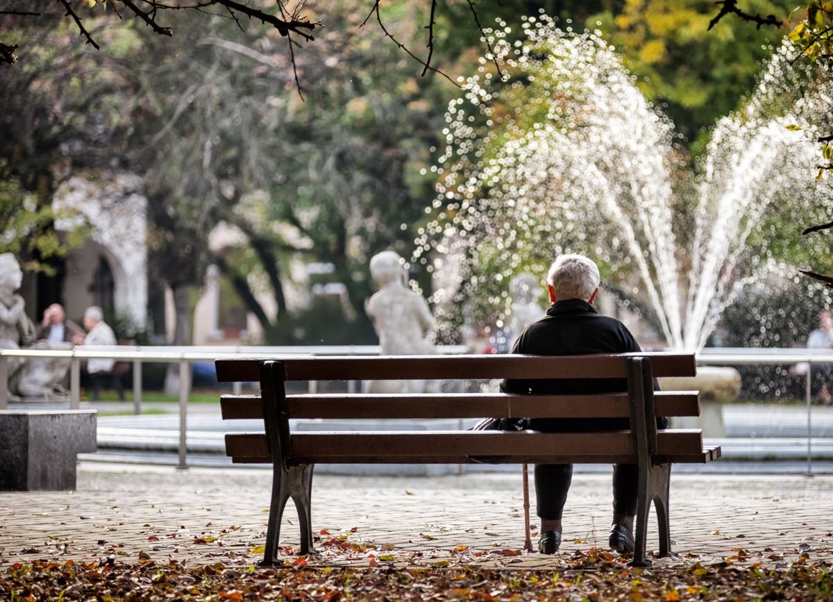 An elderly woman sits alone on a park bench.