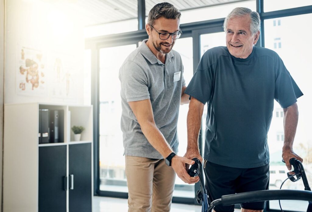 A support worker helps an elderly man using a walker.