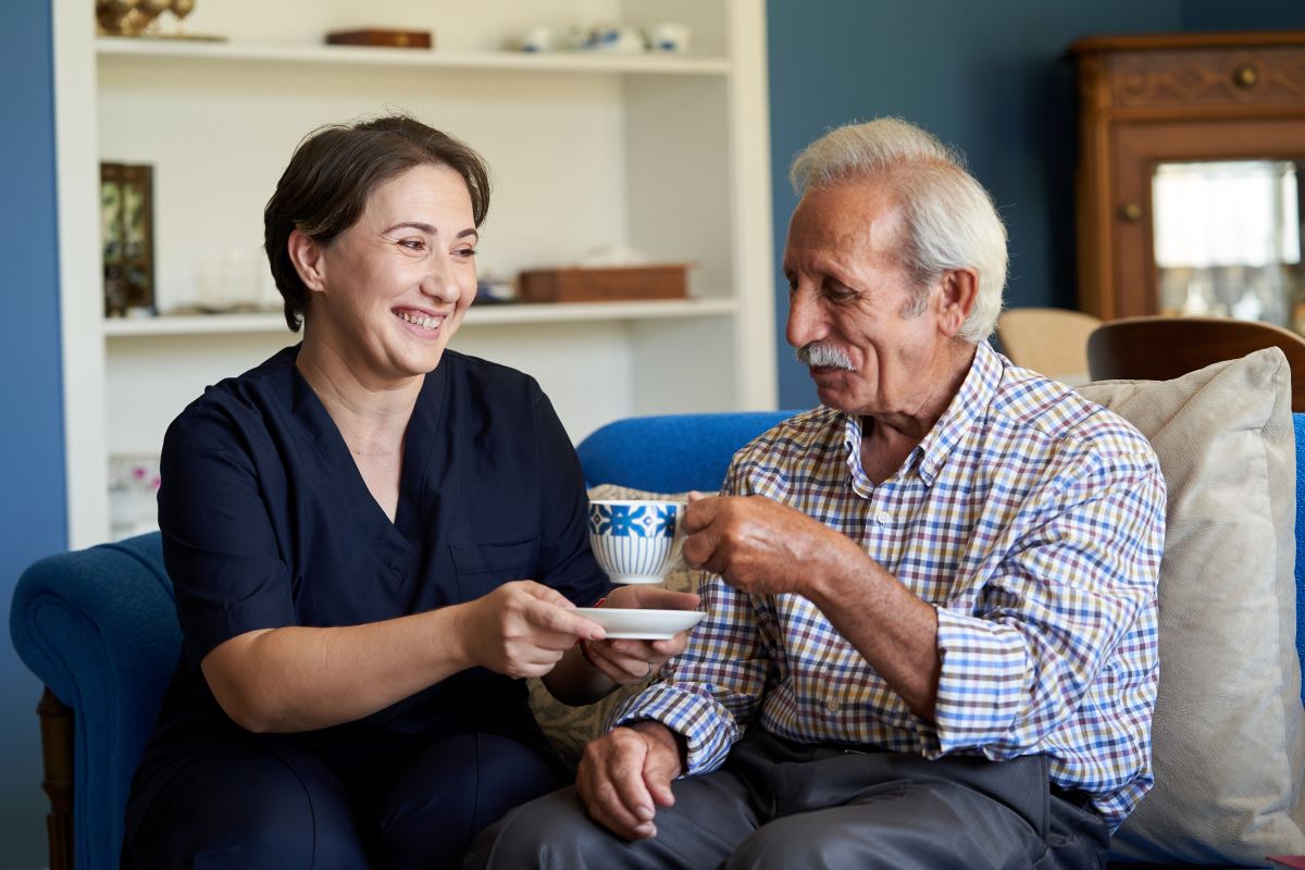 Support worker gives a smiling elderly man a cup of tea.